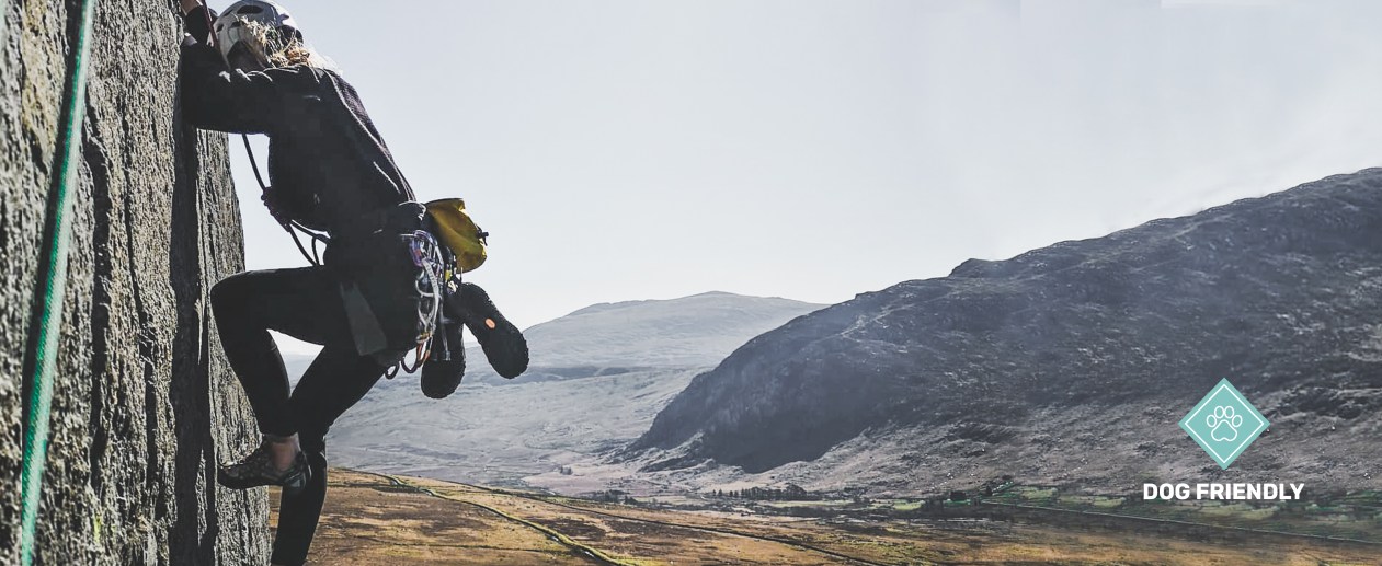 Woman climbing in the sun in North Wales, you can see the mountains in the background.