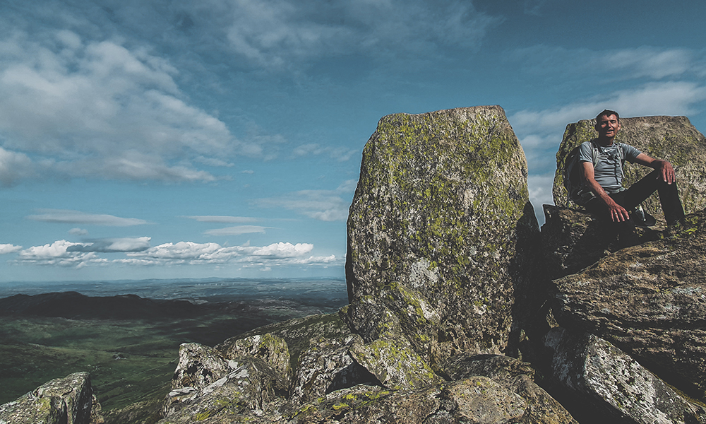 Man at the top of Tryfan Mountain, sitting on Adam and Eve