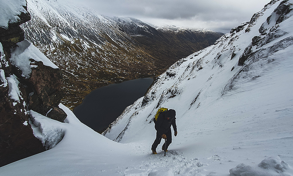 Person walking up a snowy gully in Scotland with an ice axe.