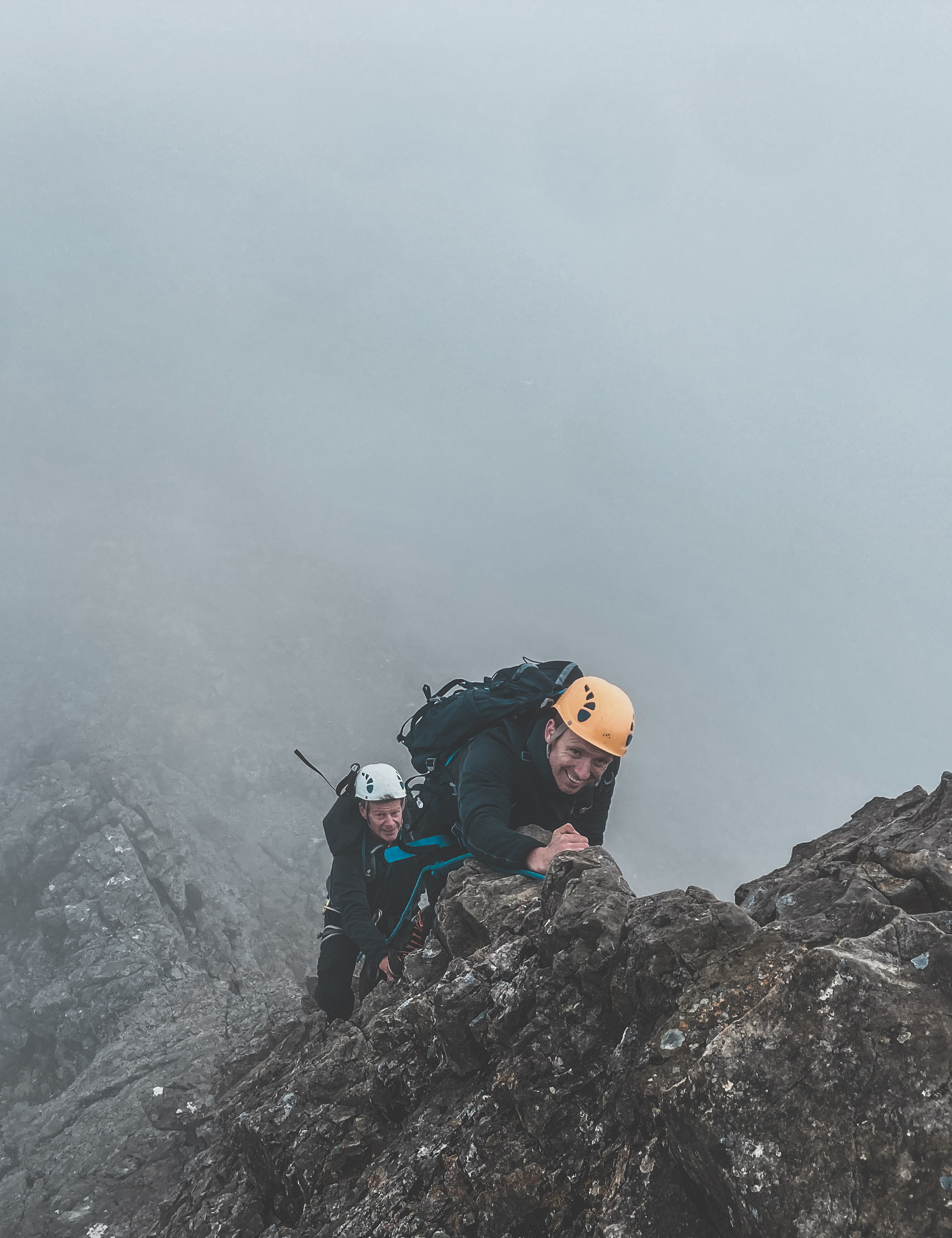 Two guys getting guided on the Cuillin Ridge in Scotland, climbing up some tricky moves.