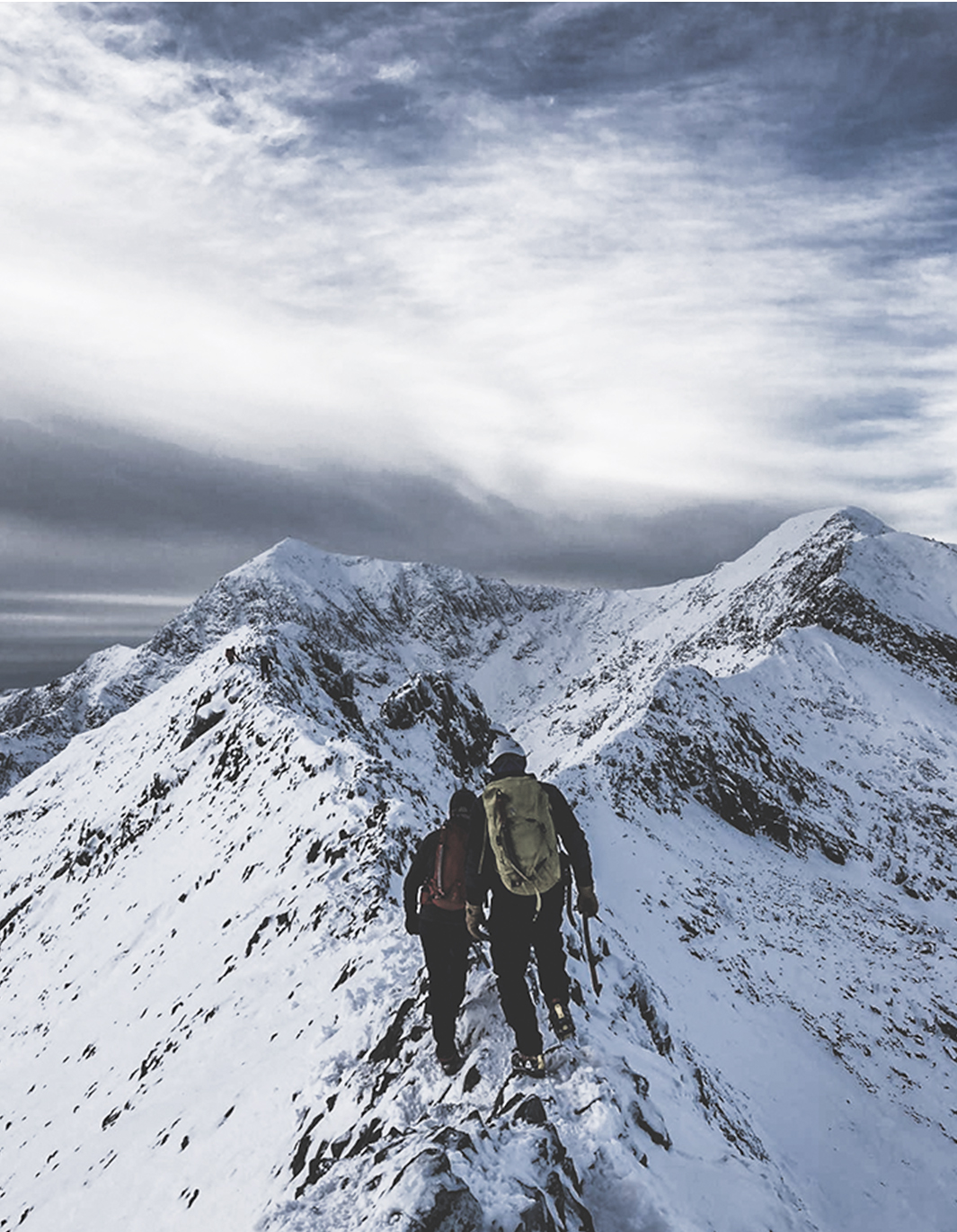 Two people walking along Crib Goch in North Wales in Winter.