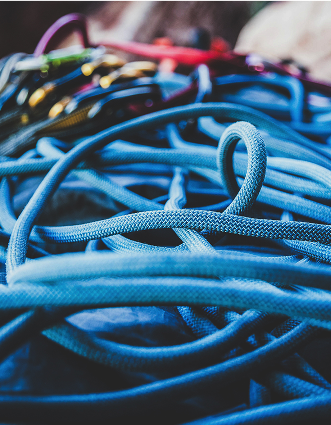A pile of rock climbing equipment lying on the floor, including a rope and quick draws.