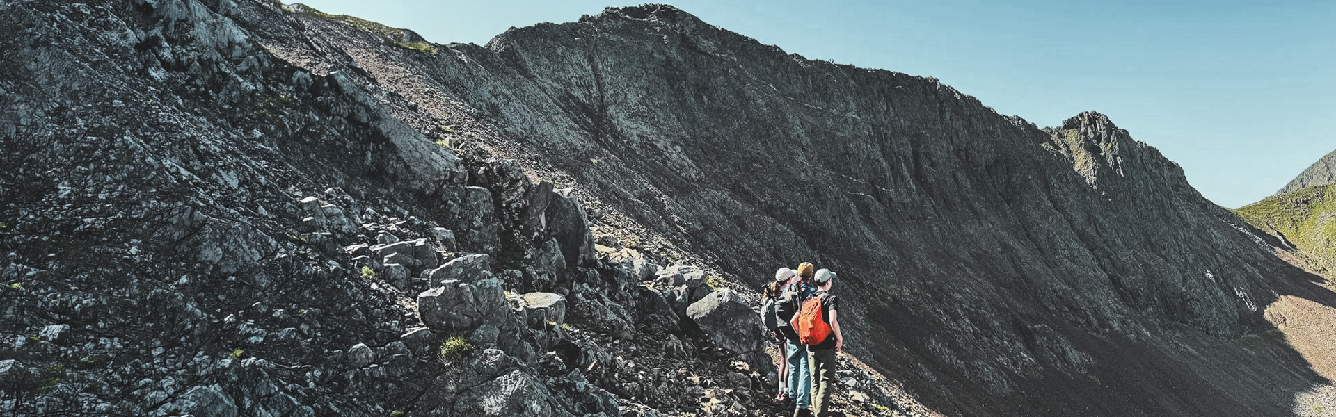 Three people looking in the distance at the start of the Crib Goch Ridge in North Wales.
